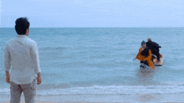 a man stands on the beach looking at a boat in the water