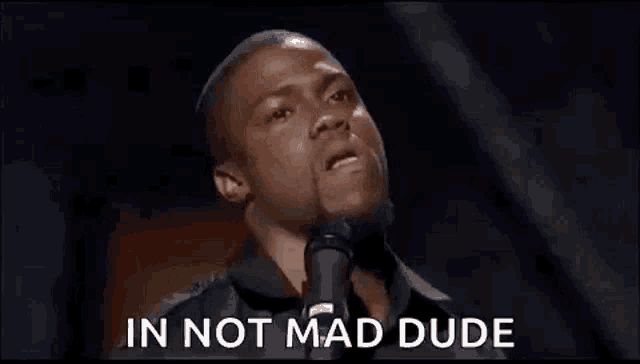 a man is standing in front of a microphone with the words `` in not mad dude '' written on the screen .