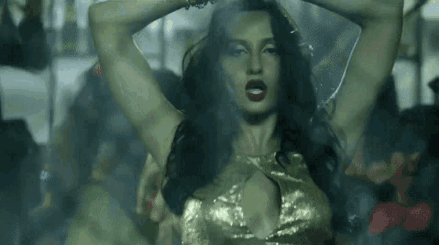 a woman in a gold top is dancing in a dark room with smoke coming out of her hair .