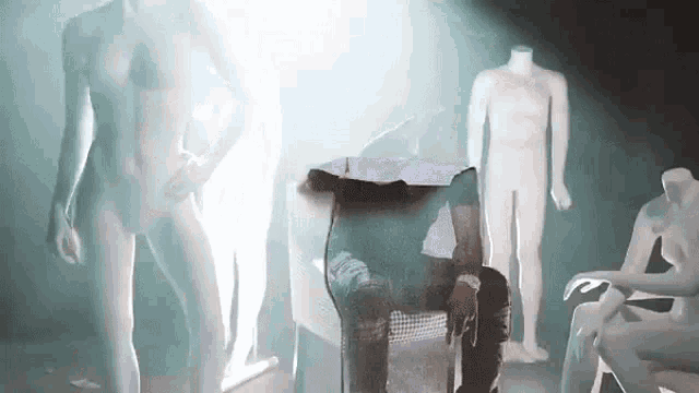 a group of mannequins are standing and sitting in a dark room .