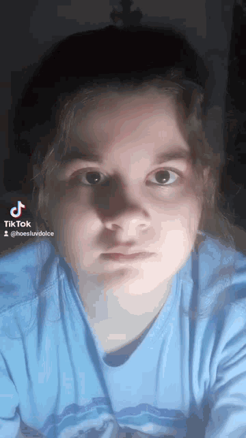 a girl wearing a blue shirt is looking at the camera and has a tiktok account