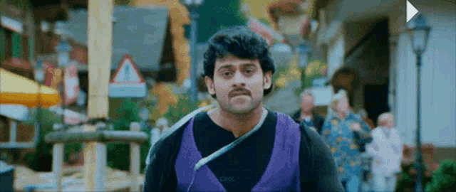 a man with a mustache is wearing a purple vest and a black shirt .