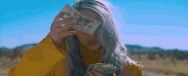 a woman in a yellow jacket is holding a bunch of money in front of her face .