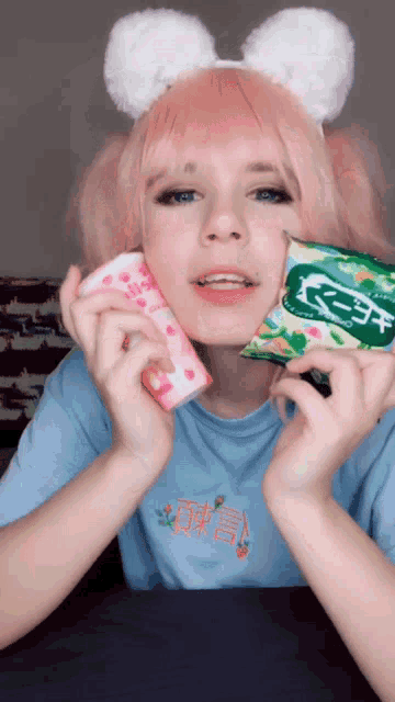 a girl with pink hair is wearing bunny ears and holding a can and a bag of chips