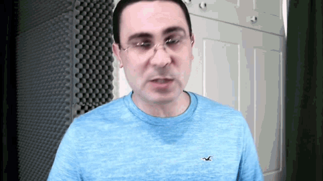 a man wearing glasses and a blue shirt with a bird on the sleeve