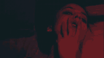 a close up of a woman 's face in a dark room with a red light behind her .