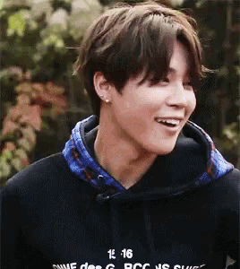 a young man wearing a black hoodie with the number 16 on it is smiling .