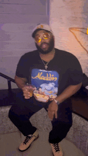 a man wearing a black shirt that says aladdin is holding a drink