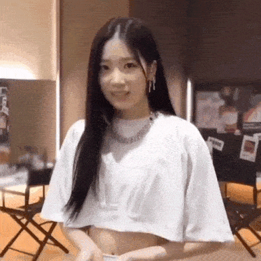 a young woman wearing a white crop top is standing in a room .