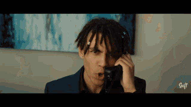 a man with dreadlocks is talking on a phone in front of a painting