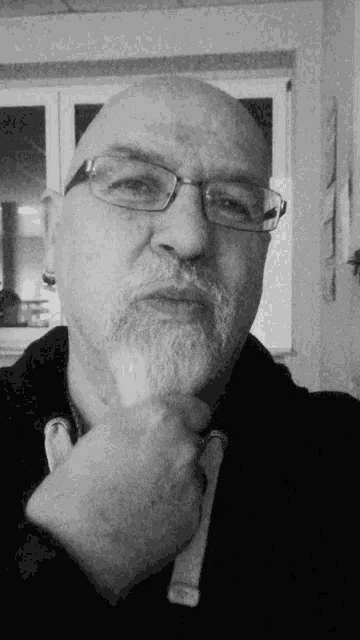 a man with glasses and a beard holds his hand to his chin in a black and white photo