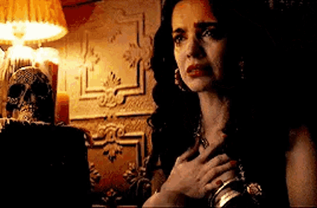 a woman is crying in a dark room with a skull and candles in the background .