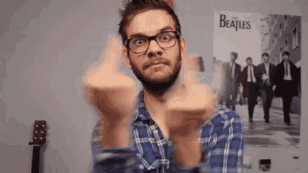 a man wearing glasses is giving the middle finger in front of a beatles poster