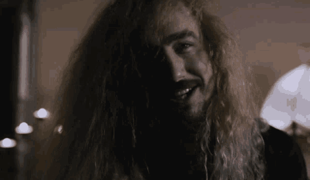 a man with long blonde hair and a beard is smiling and looking at the camera .