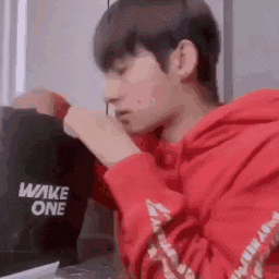 a young man in a red hoodie is sitting in front of a laptop computer .