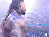 roman reigns is standing in front of a wrestling ring in a wrestling ring .
