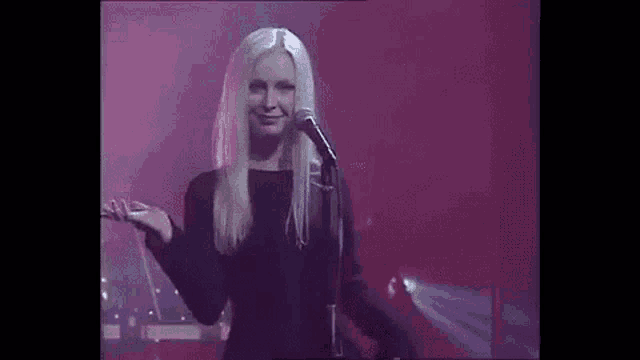 a woman in a black dress is singing into a microphone on stage .