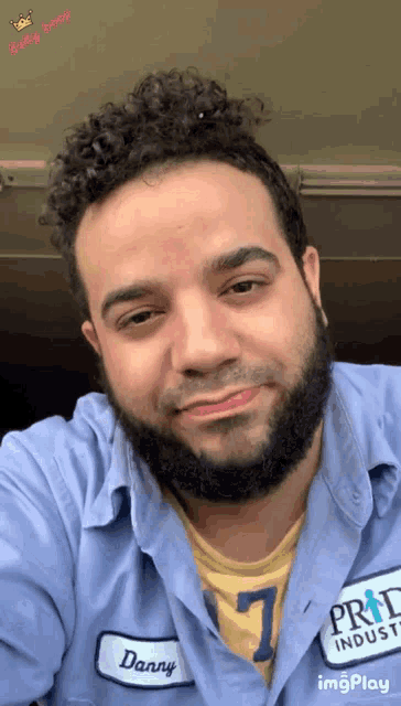 a man with a beard wears a blue shirt with a patch that says danny on it
