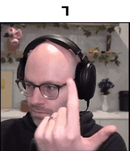 a bald man wearing headphones and glasses is making a middle finger sign .