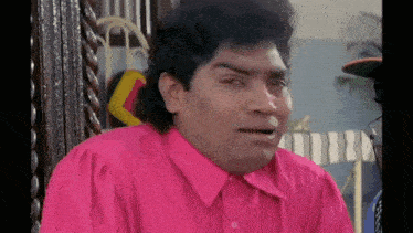 a man in a pink shirt is making a funny face while sitting on a chair .