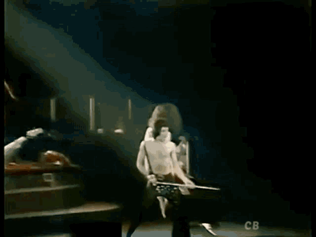 a man is playing a guitar on a stage while another man stands behind him .