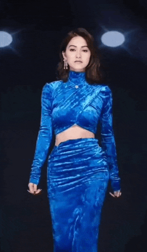 a woman is walking down a runway wearing a blue velvet dress .