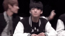 a man in a black and white jacket is sitting in front of a group of people and making a funny face .