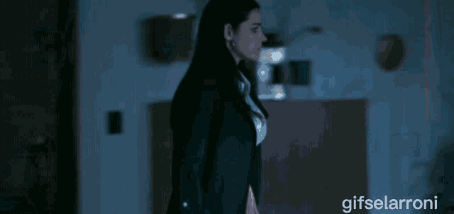 a woman in a black jacket is standing in a dark room with gifselaroni written on the bottom