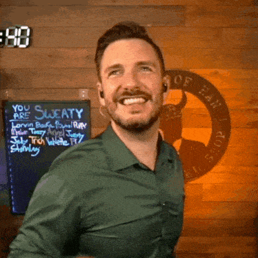 a man in a green shirt smiles in front of a sign that says you are sweaty