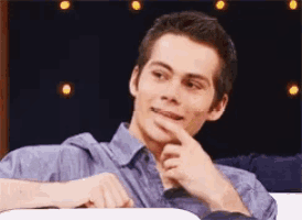 a young man in a blue shirt is smiling with his finger on his chin