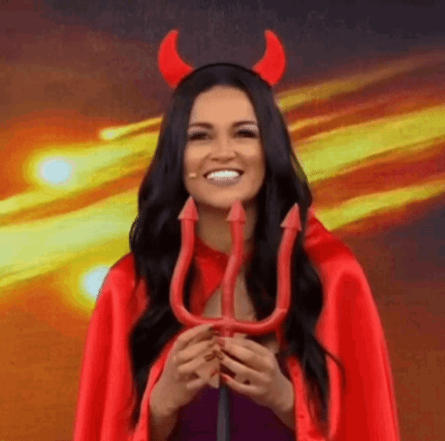 a woman dressed as a devil is holding a trident and horns .