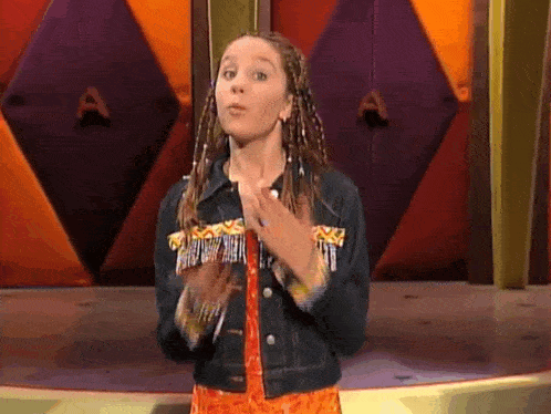 a young girl with braids and a denim jacket is standing in front of a colorful wall .