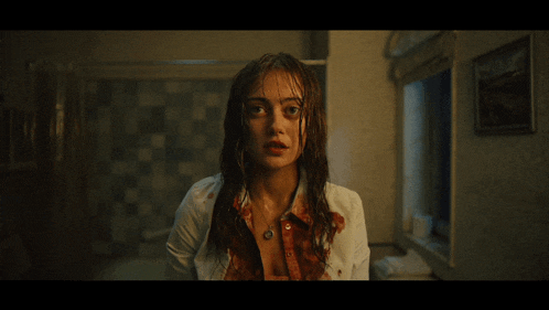 a woman with blood on her shirt is standing in a bathroom looking at the camera
