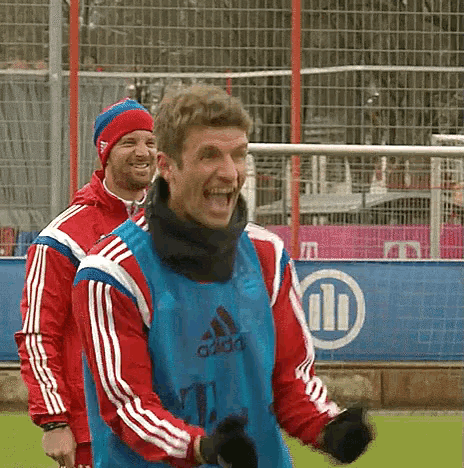 a man wearing a blue adidas vest laughs on a soccer field