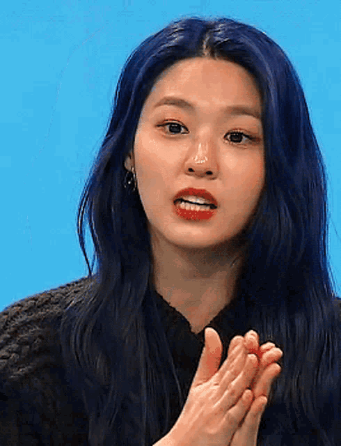 a woman with blue hair and red lips is clapping her hands
