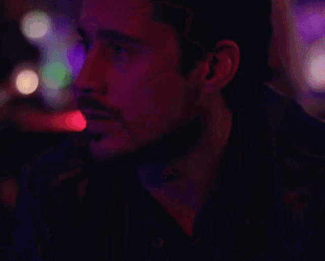 a close up of a man 's face with a beard in a dark room with purple lights .
