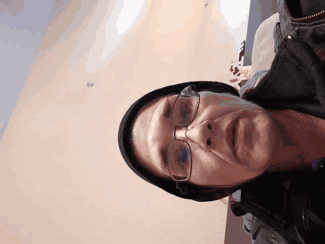 a man wearing glasses and a beanie looks down at something