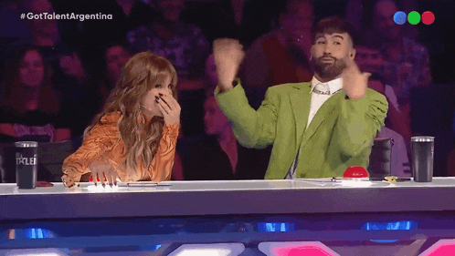 a man in a green suit applauds while a woman laughs in front of a screen that says gottalentargentina