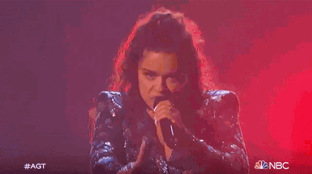 a woman is singing into a microphone on a stage with a purple background .