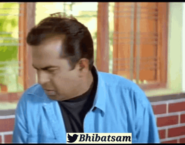 a man in a blue shirt is standing in front of a brick wall and a window ..