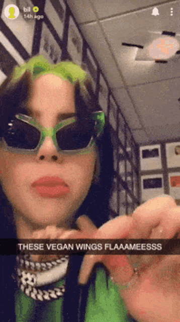 billie eilish is wearing green sunglasses and making a face