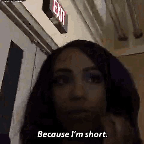 a woman is standing in front of an exit sign and saying because i 'm short