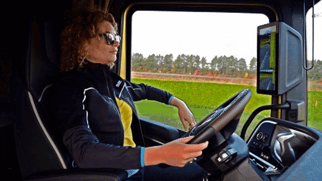 a woman wearing sunglasses is driving a truck with a steering wheel that says volvo on it