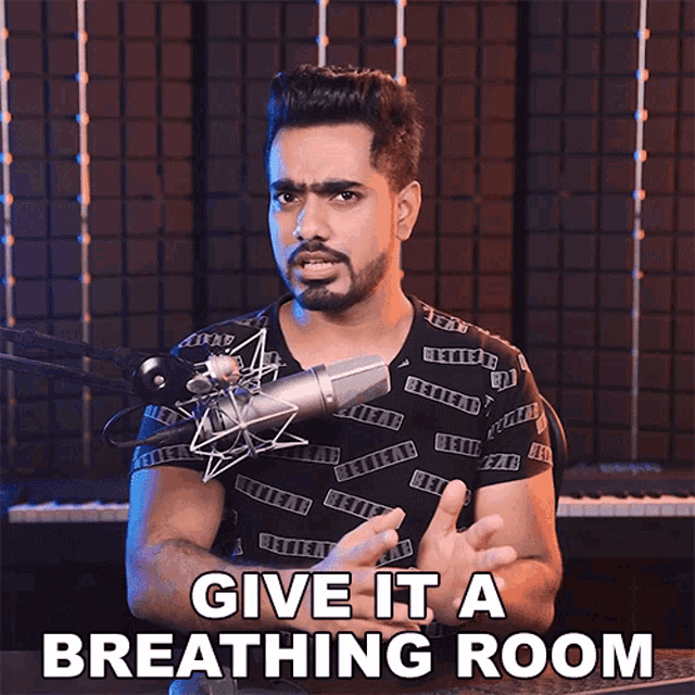a man stands in front of a microphone with the words give it a breathing room above him