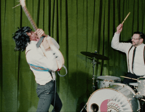 a man playing drums while another man plays guitar