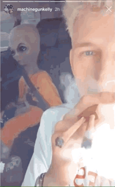 a man is smoking a cigarette in a car with an alien in the background