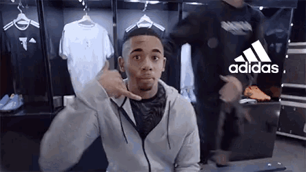 a man is pointing at something in a locker room with the adidas logo on the wall behind him