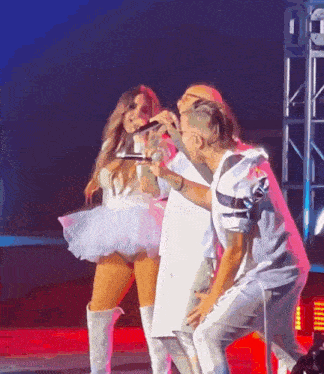 a woman in a white tutu is singing into a microphone while two men watch