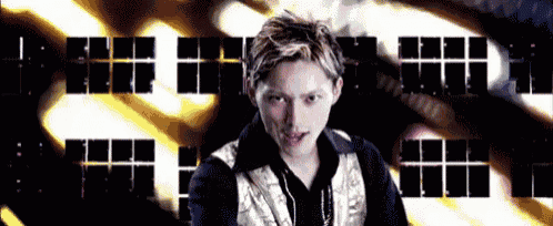 a young man in a black and gold jacket is standing in front of a building with squares on it .