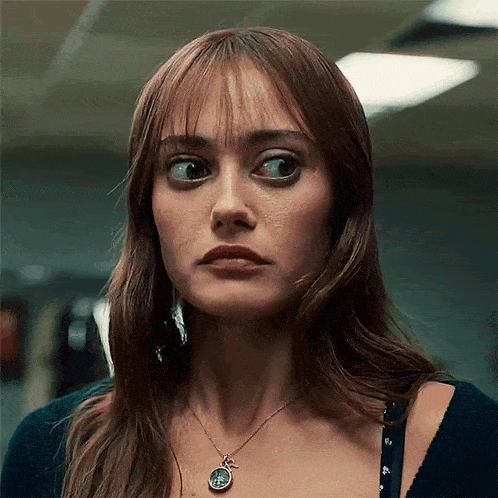 a close up of a woman 's face with a necklace that has a coin on it